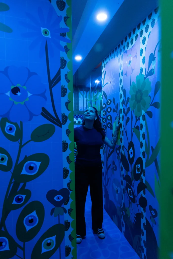 A visitor exploring a blue-lit floral mirror illusion room at Mind Games Sydney, surrounded by reflective walls and oversized flower patterns.