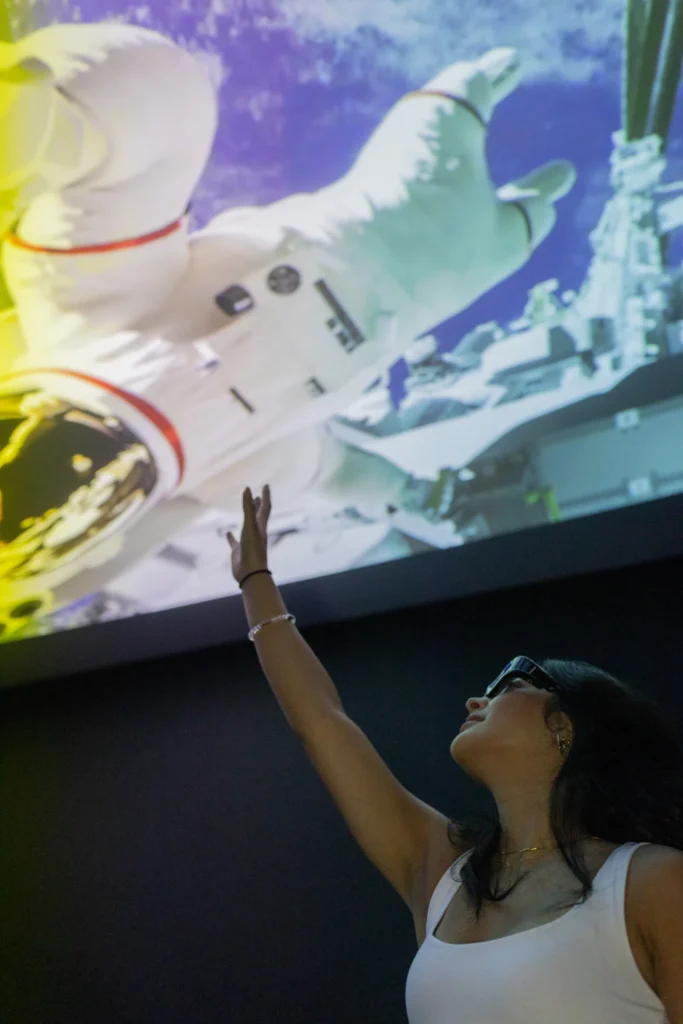 A visitor reaching toward an astronaut projection in an immersive space-themed room at Mind Games Sydney.