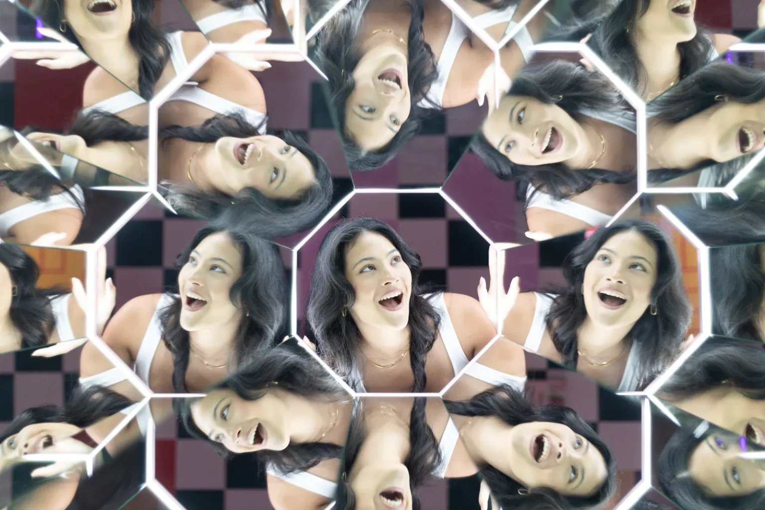 A visitor surrounded by multiple reflections in a geometric kaleidoscope mirror illusion at Mind Games Sydney.